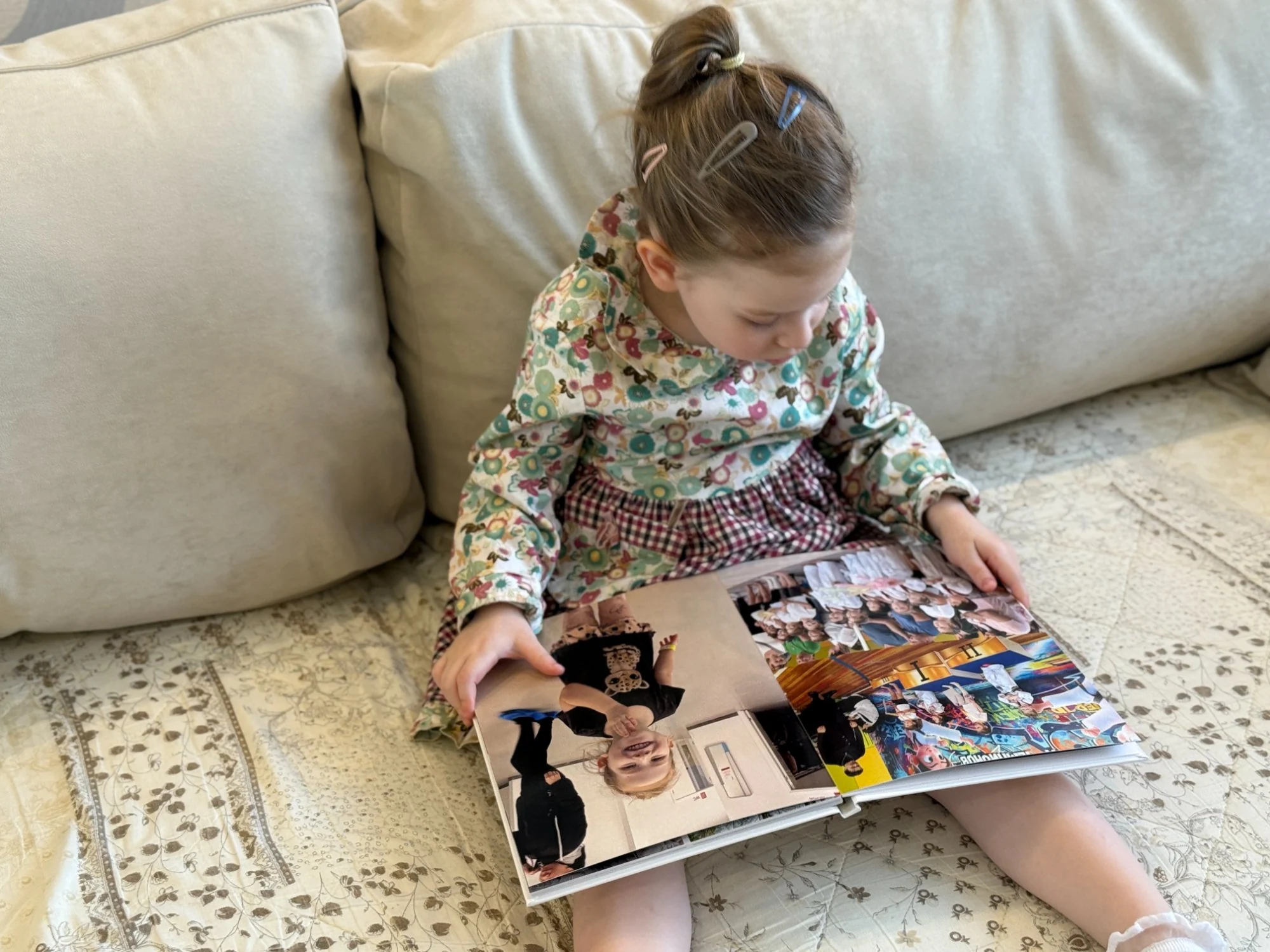 Девочка самостоятельно листает детскую фотокнигу на диване
